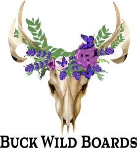 Buck Wild Boards logo featuring a deer skull with antlers adorned with a floral crown of purple flowers, lavender, green leaves, and purple butterflies