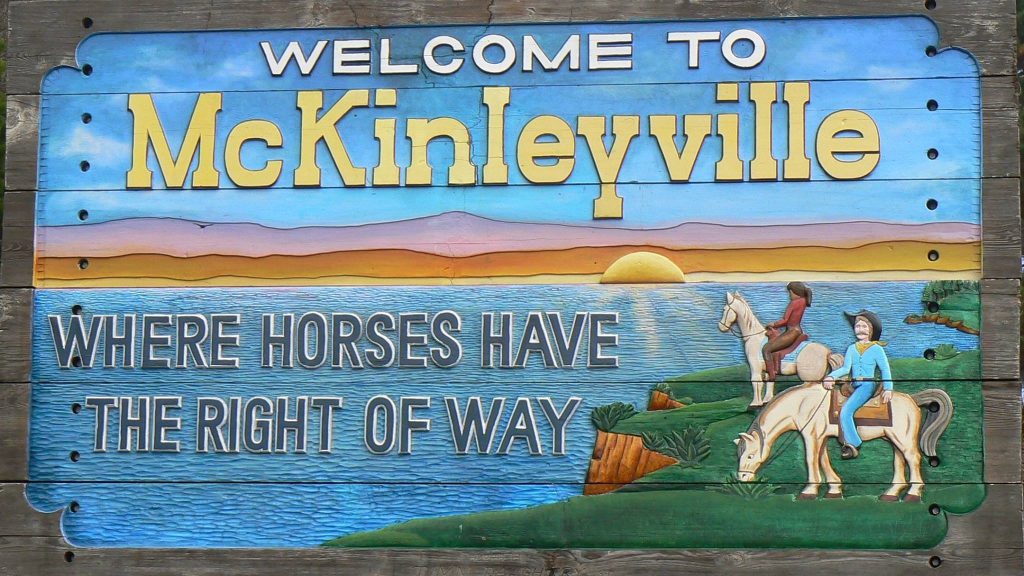 Welcome to McKinleyville sign with coastal scenery and horseback riders.