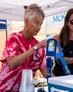 A community volunteer wearing a pink Pony Express Days tie-dye shirt pours a beer from a Six Rivers Brewery tap handle at an outdoor community event