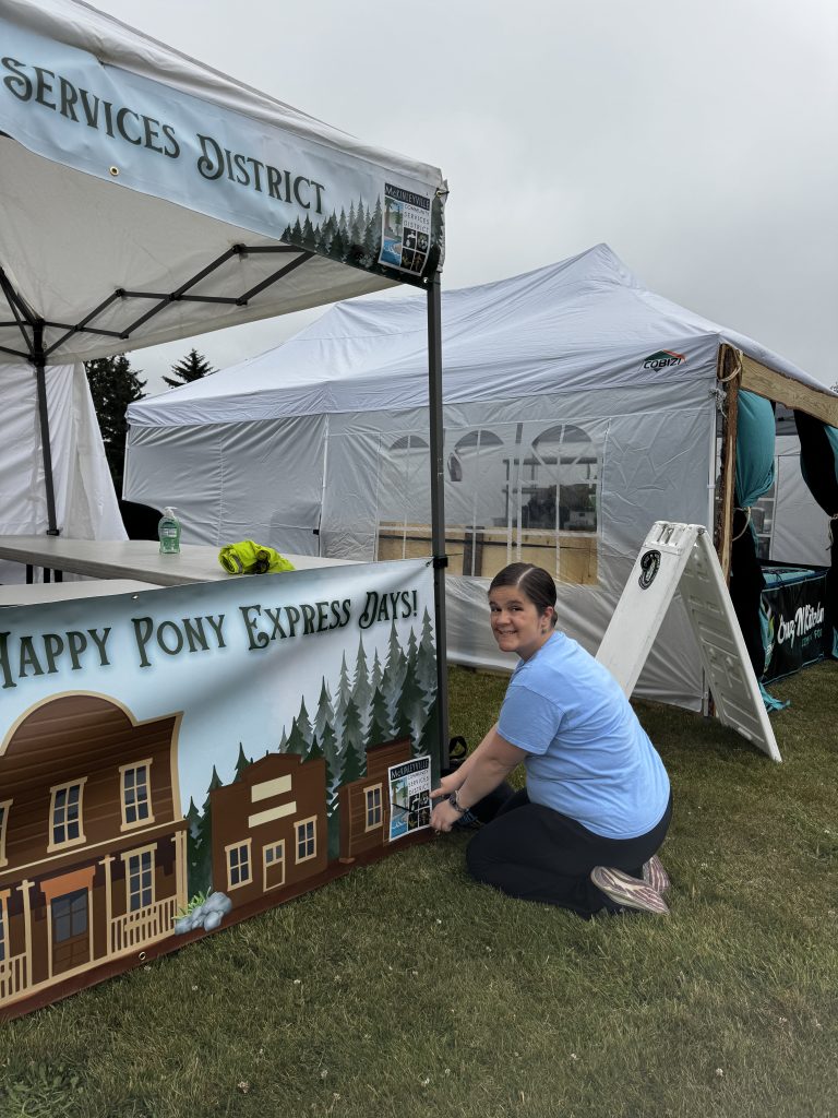 A volunteer or staff member setting up a Pony Express Days booth near community partner tents in McKinleyville.