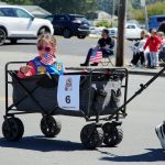 Young Parade Participant – Pony Express Days 2026 A young parade participant rides in a wagon while waving American flags during the Pony Express Days 2026 Parade in McKinleyville, California.