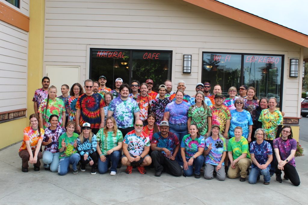 Tie‑Dye Group Photo at Natural Café Large group wearing colorful tie‑dye shirts posing outside a building with Natural Café and Espresso signs.