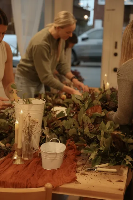 Floral Arrangement Workshop People arranging greenery and candles on a table during a floral design workshop.